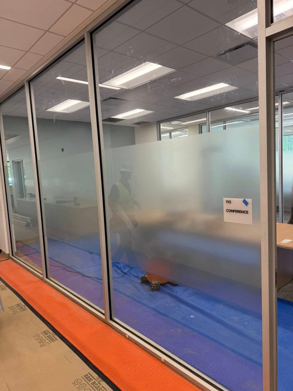 Frosted glass conference room under construction with worker and equipment.
