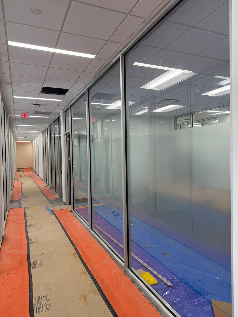 Renovated office hallway with glass partitions and orange protective flooring.