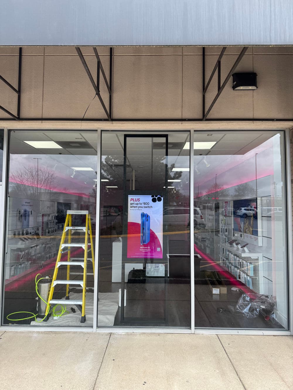 New storefront with ladder and promotional poster for Plus products in a retail location.